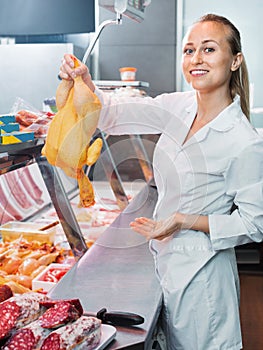 Young woman seller holding fresh whole chicken