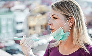 Young woman sending voice message outdoor during isolation quarantine - Girl using social app while wearing face mask and latex