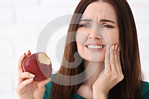 Young woman with sensitive teeth and apple on blurred background