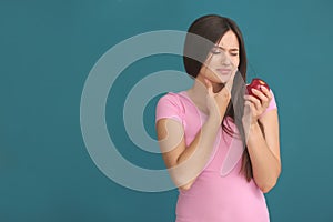 Young woman with sensitive teeth and apple on color background