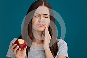 Young woman with sensitive teeth and apple on color background