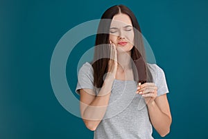 Young woman with sensitive teeth and cold ice cream on color background