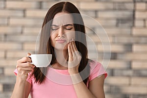 Young woman with sensitive teeth and cup of hot coffee on blurred background