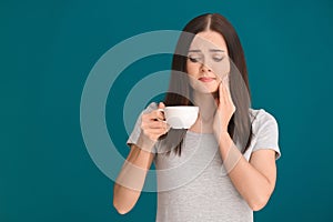 Young woman with sensitive teeth and cup of hot coffee on color background