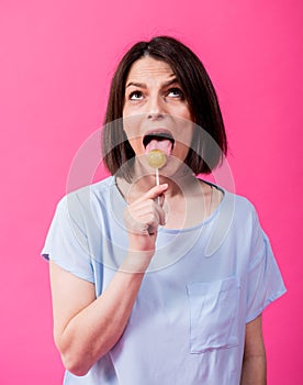 Young woman with sensitive teeth eating sweet lollipop on color background