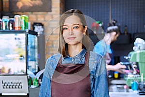 Young woman service worker in apron looking at camera in restaurant, coffee shop