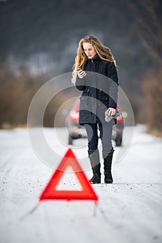 Young woman setting up a warning triangle and calling for assistence