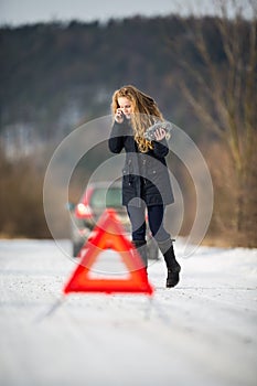 Young woman setting up a warning triangle and calling for assistence