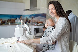 A young woman sews in the kitchen and holds a small child. Mom teaches her little son to sew on a sewing machine. Self