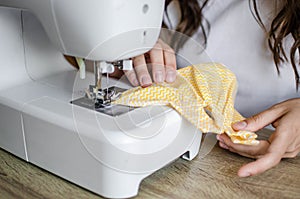 Young woman sews a small yellow dress for Barbie toys on a sewing machine.