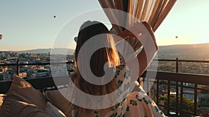 Young woman shakes her hair and stretches during sunrise with amazing view of hot air ballons in Cappadocia