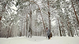 Young woman shaking tree with snow falling in winter forest