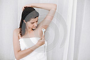 Young woman shaving armpits with plastic razor closeup in home bathroom. Skin care. Hair Removal concept. Copy space. Hand holding