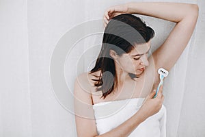 Young woman shaving armpits with plastic razor closeup in home bathroom. Skin care. Hair Removal concept. Copy space. Hand holding