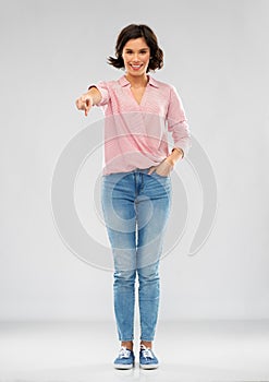 Young woman in shirt and jeans pointing to you