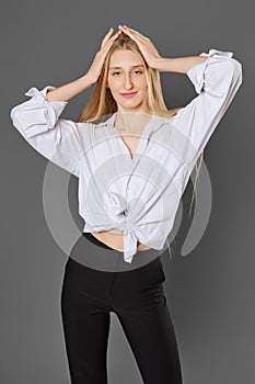 Young woman in a shirt tied at the waist posing with her hands raised to her head