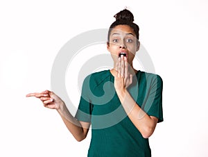 Young woman with shocked expression pointing at copy space