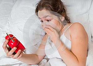 Young woman is shocked by looking at clock. She is late and oversleep photo