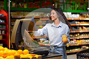 Young woman shopper in supermarket uses self-service scales, smiling Hispanic woman weighs fruits and vegetables in