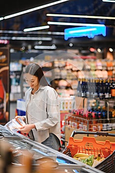 Young woman with a shopping bag as a customer buying fish at the refrigerated shelf in the supermarket