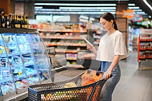 Young woman with a shopping bag as a customer buying fish at the refrigerated shelf in the supermarket