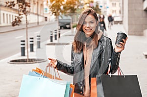 Young woman with shopping bags and coffee walking outdoors. Happy lifestyle, holiday discounts and sales