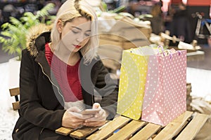 Young woman with shopping bags sitting in cafe at shopping mall. Girl with a phone in her hand