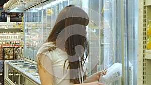 Young woman with shopping cart buying dairy or refrigerated groceries at the supermarket in the refrigerated section