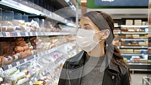 Young woman shopping in grocery store for food while wearing mask and preventing spread of coronavirus virus germs by wearing face
