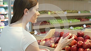 Young woman shopping in grocery store for healthy food. Vegan girl choosing fresh red apples