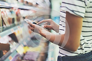 Young woman shopping healthy food in supermarket blur background. Close up view girl buy products using smartphone in store
