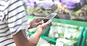 Young woman shopping healthy food in supermarket blur background. Close up view girl buy products using smartphone in store