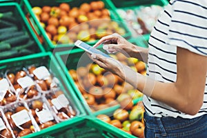 Young woman shopping healthy food in supermarket blur background. Female hands buy nature products using smart phone in store
