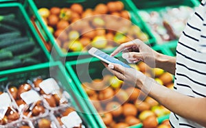 Young woman shopping healthy food in supermarket blur background. Female hands buy nature products using smart phone in store