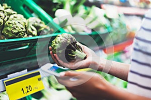 Young woman shopping healthy food in supermarket blur background. Female hands buy products artichoke using smartphone in store