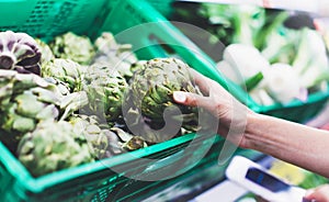 Young woman shopping healthy food in supermarket blur background. Female hands buy products artichoke using smartphone in store