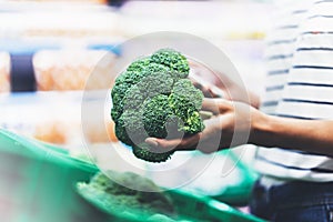 Young woman shopping healthy food in supermarket blur background. Female hands buy products broccoli using smartphone in store