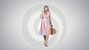 Young woman shopping and making a phone call while walking on gradient background.