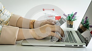 A young woman shopping online through a laptop and her hand holding a credit