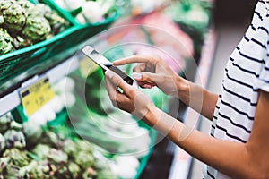 Young woman shopping purchase healthy food in supermarket blur background. Close up view girl blogger buy products using smartphon