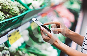 Young woman shopping purchase healthy food in supermarket blur background. Close up view girl buy products using smartphone in sto