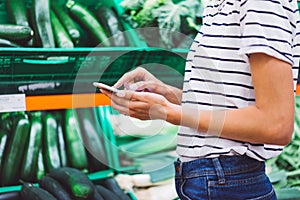 Young woman shopping purchase healthy food in supermarket blur background. Close up view girl buy products using smartphone in sto