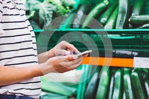 Young woman shopping purchase healthy food in supermarket blur background. Close up view girl buy products using smartphone in sto