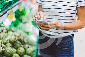 Young woman shopping purchase healthy food in supermarket blur background. Close up view girl buy products using smartphone in sto