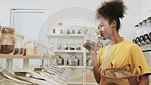 A young woman is shopping in refill store with reusable bag, zero-waste grocery.