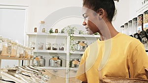 A young woman is shopping in refill store with reusable bag, zero-waste grocery.