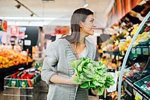 Young woman shopping in the supermarket grocery store for fresh greens.Buying organic vegetables sustainable produce.Natural