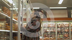 Young woman shopping at supermarket. Opening fridge to pick up refrigerated food