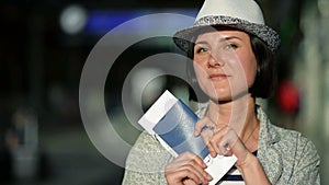 Young Woman with Short Dark Hair and Summer Hat Holding Her Passport and Ticket is Looking at the Camera and Smiling at