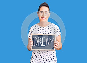 Young woman with short hair holding blackboard with dream word looking positive and happy standing and smiling with a confident